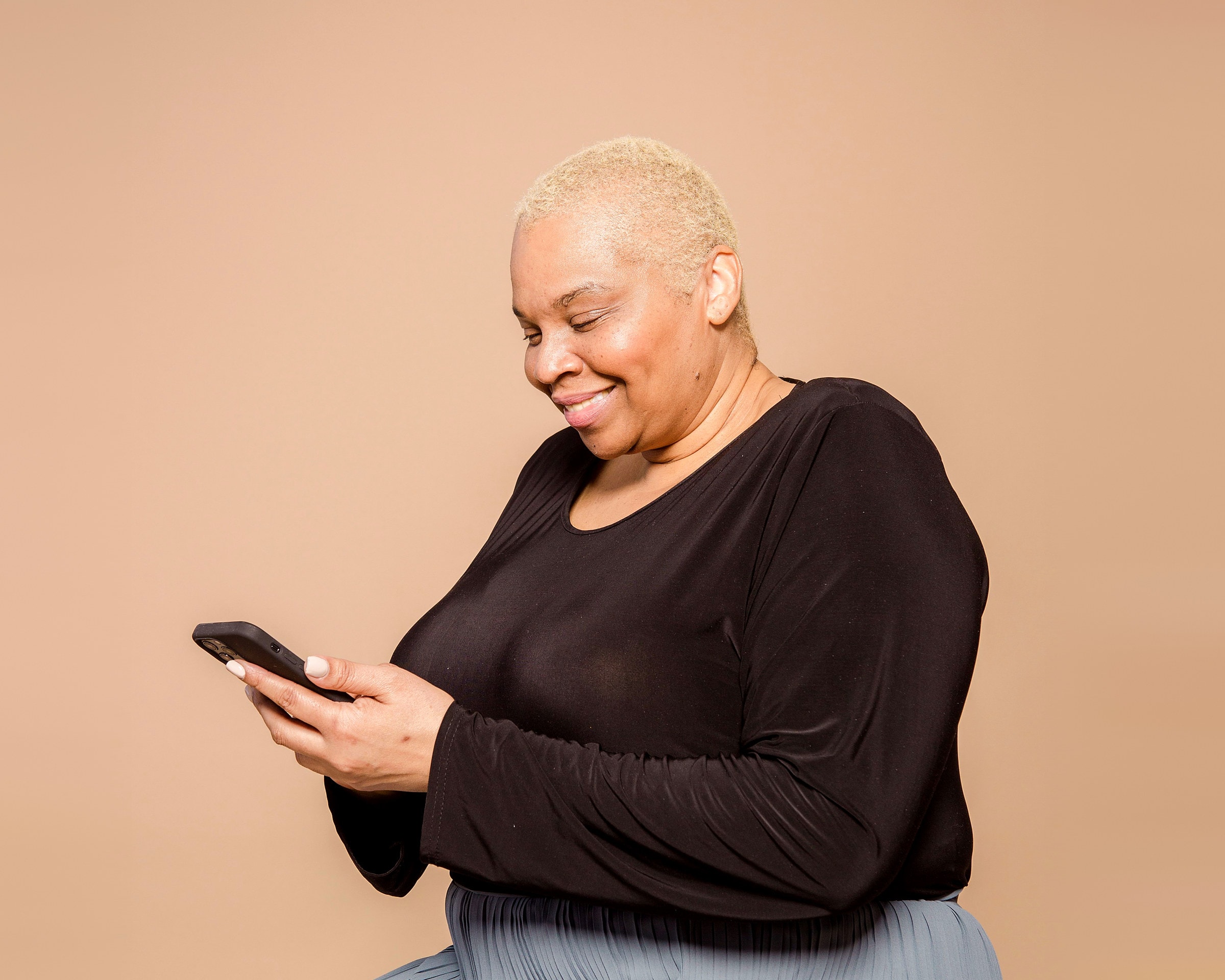 An older woman with short white hair smiling as she reads a message on her phone